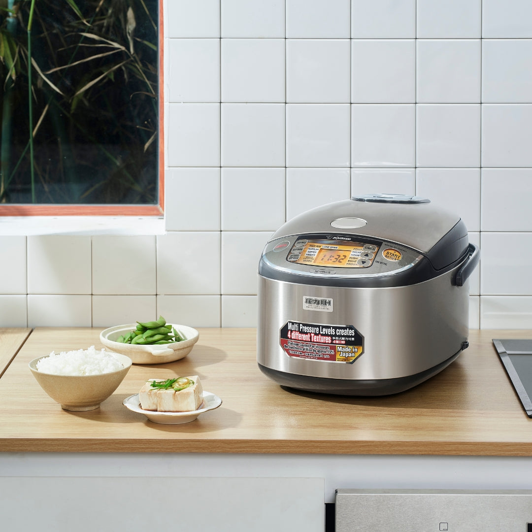 Zojirushi Rice Cooker UAE on kitchen counter with rice, greens, and a plate of bread.