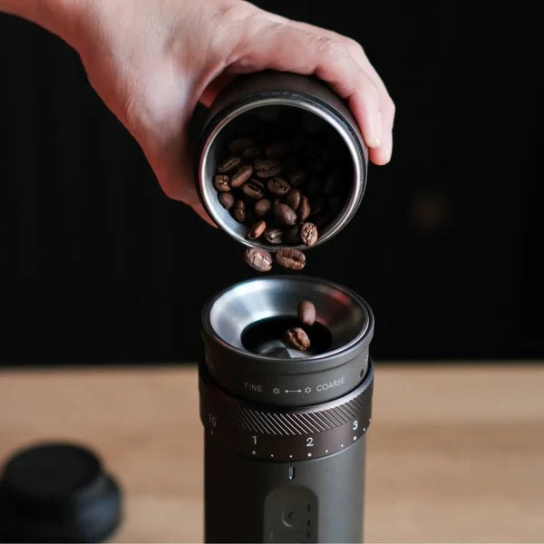  adding beans to Outin Fino portable electric coffee grinder in tundra brown finish.