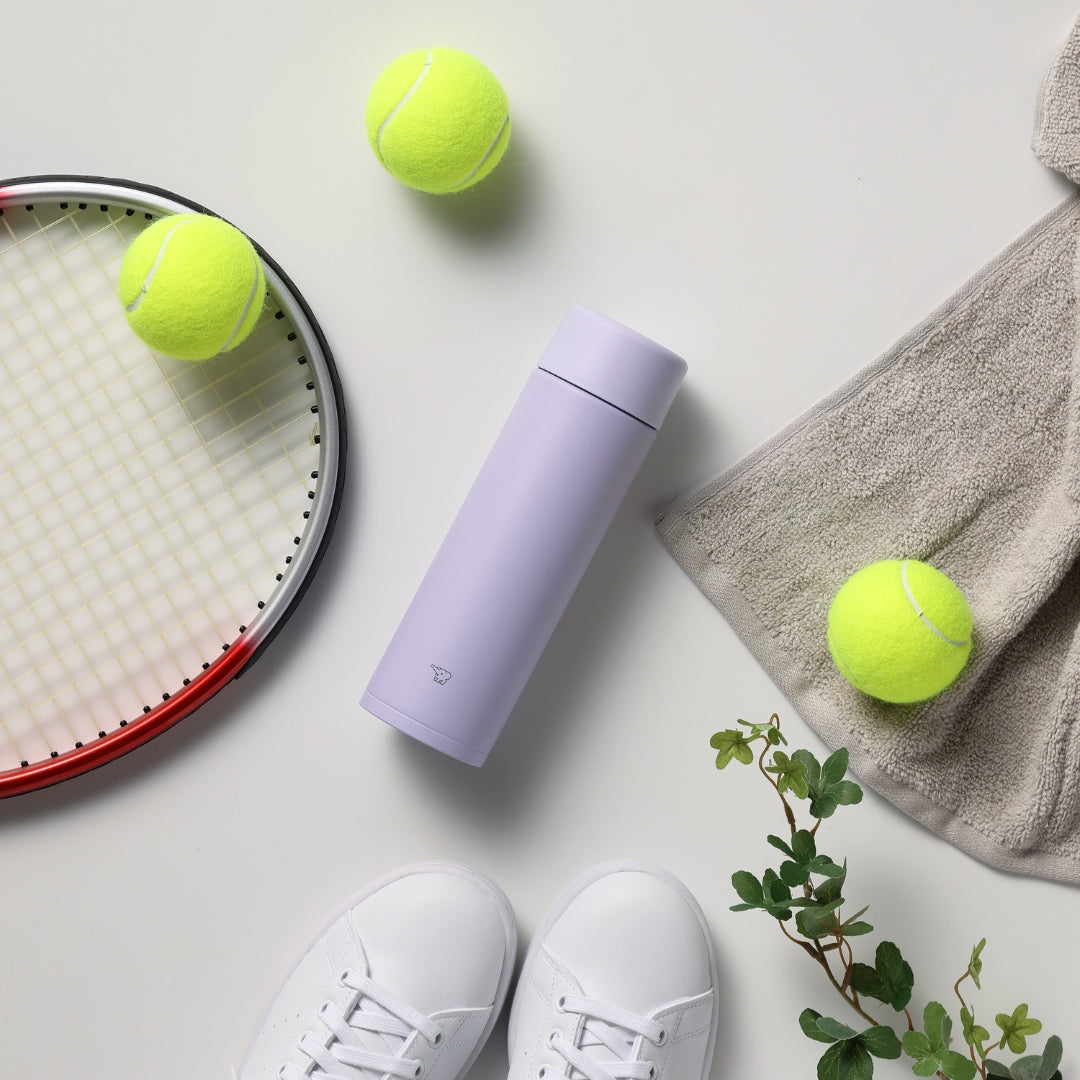 Purple water bottle with tennis balls, racket, and sneakers on a light surface