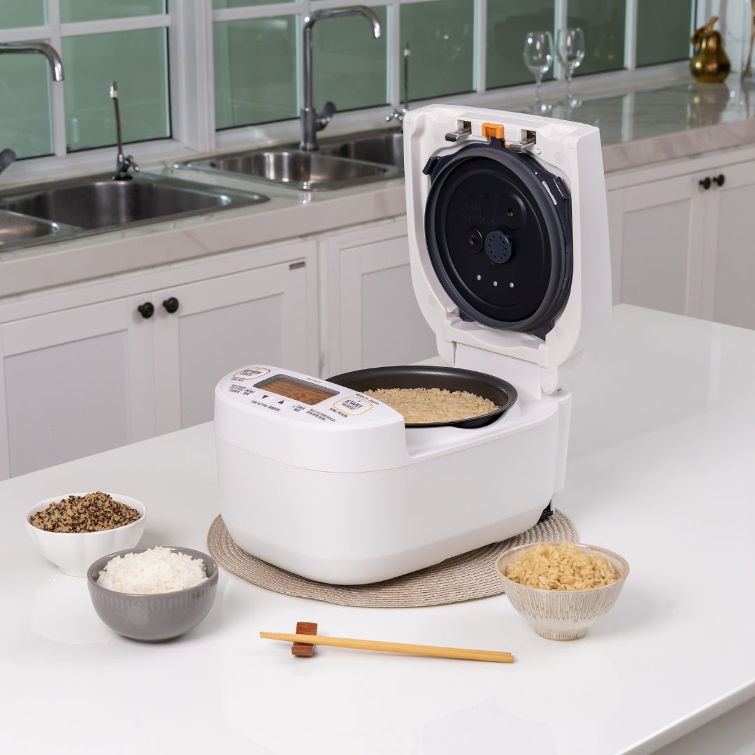 White rice cooker on a kitchen counter with various ingredients around it.