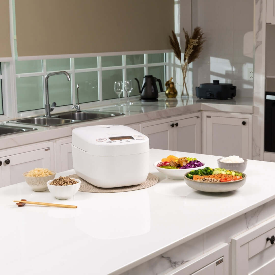 White rice cooker on a kitchen counter with various dishes and utensils.